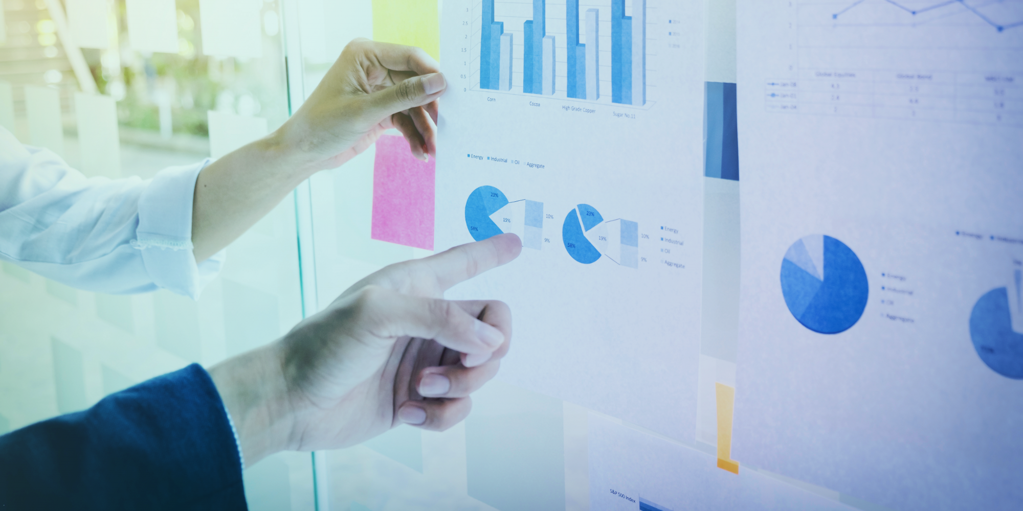 Businesspeople pointing at pie charts and graphs taped to a glass wall